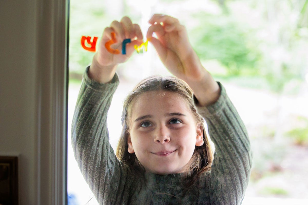 Young girl placing Hebrew letters on a glass door in joyful concentration, reflecting Jewish community impact in Boston through Jewish life and learning.