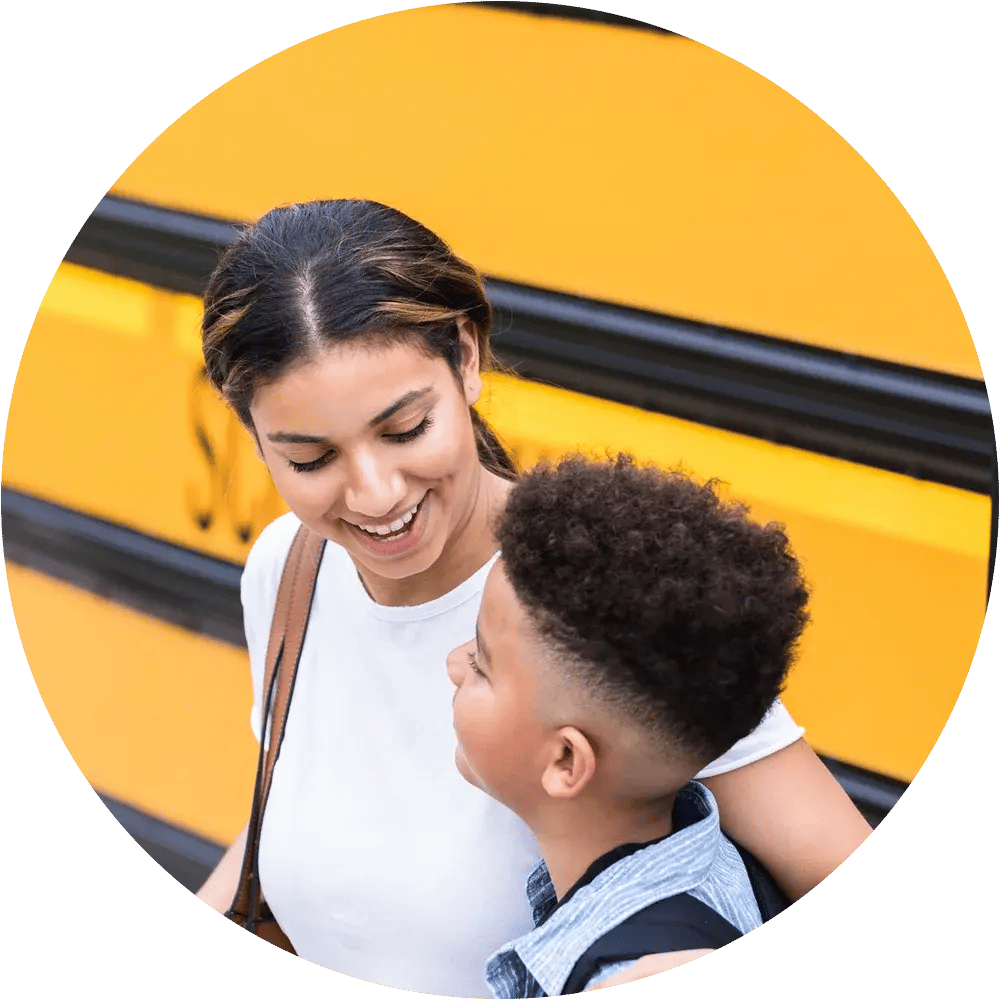 Parent and child standing near a school bus.