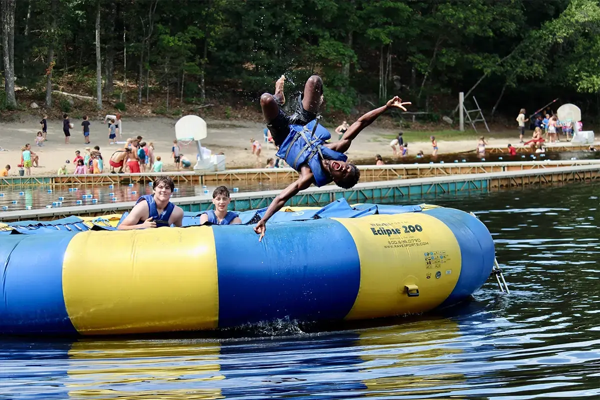 A preteen kid is jumping off a floating raft in a lake with his friends at Jewish summer camp.