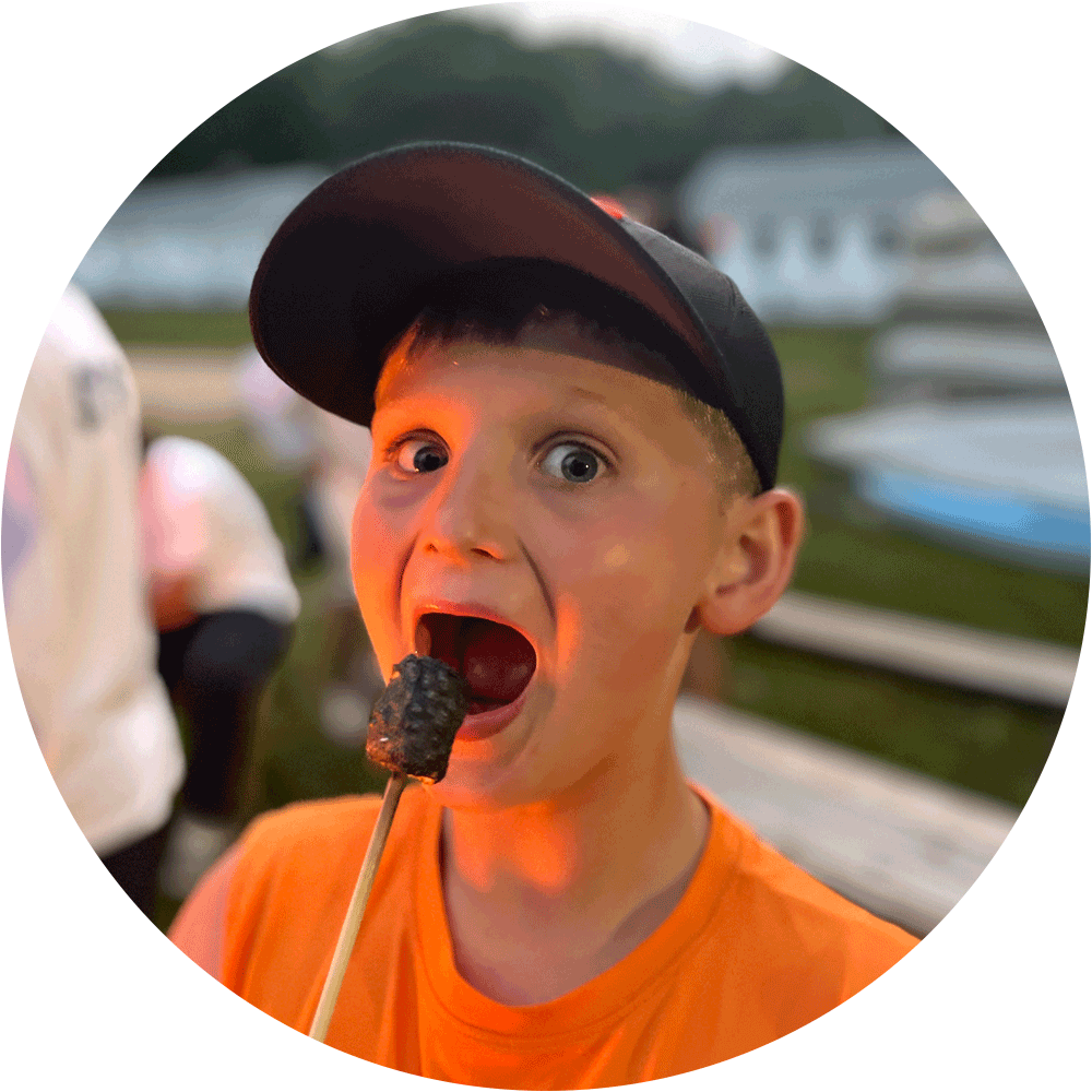 Jewish life Boston summer camp moment with a young boy roasting a marshmallow by the fire, capturing joy and outdoor traditions in Greater Boston.