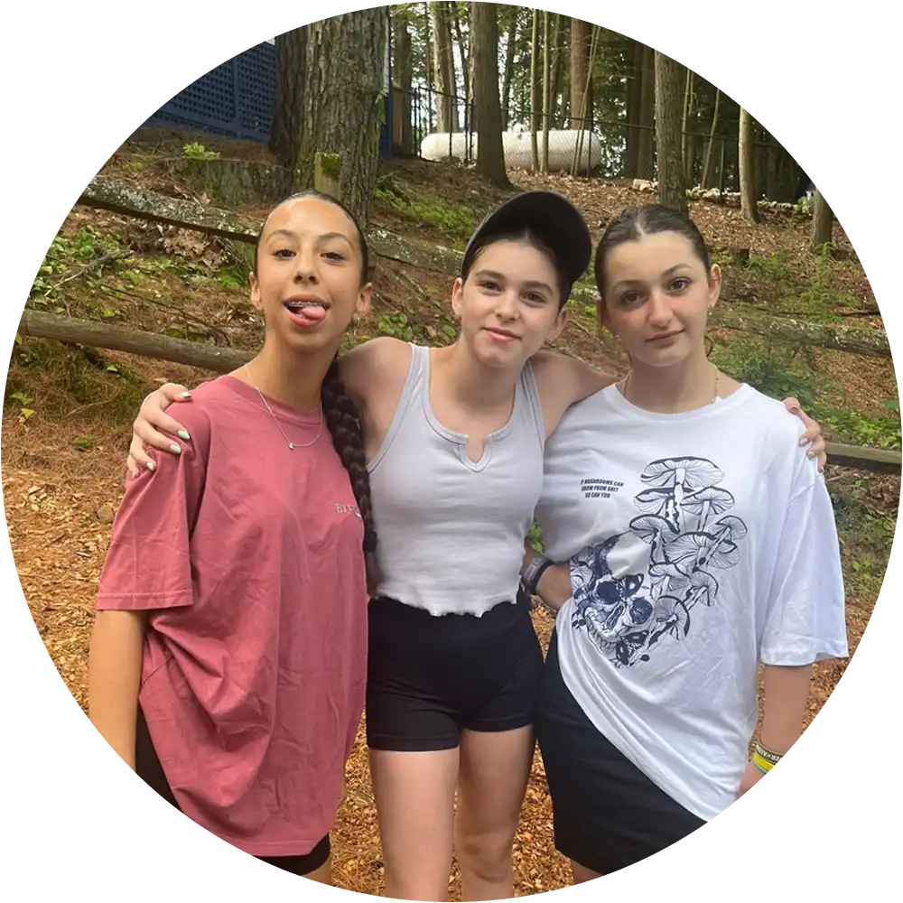 Three children standing arm in arm in the woods at summer camp.
